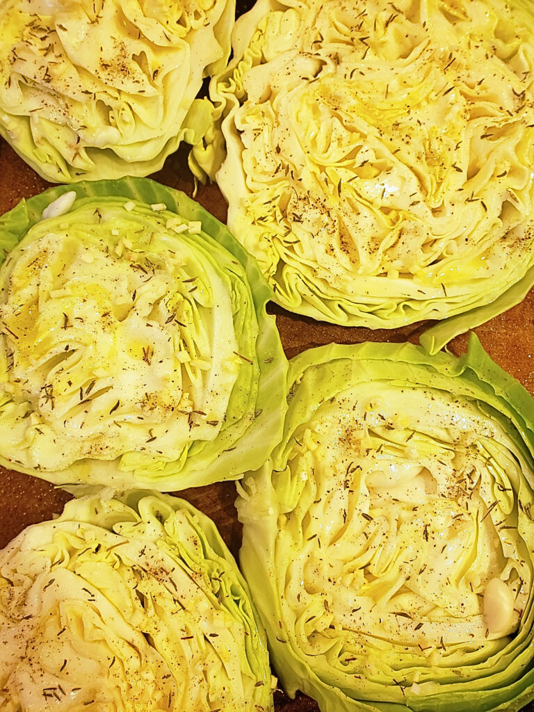 Close-up shot of prepped cabbage steak recipe on a baking sheet with oil, garlic, and seasonings on top.