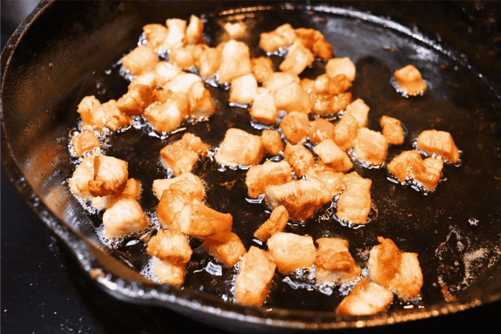 Cubed pork belly frying in a cast iron skillet