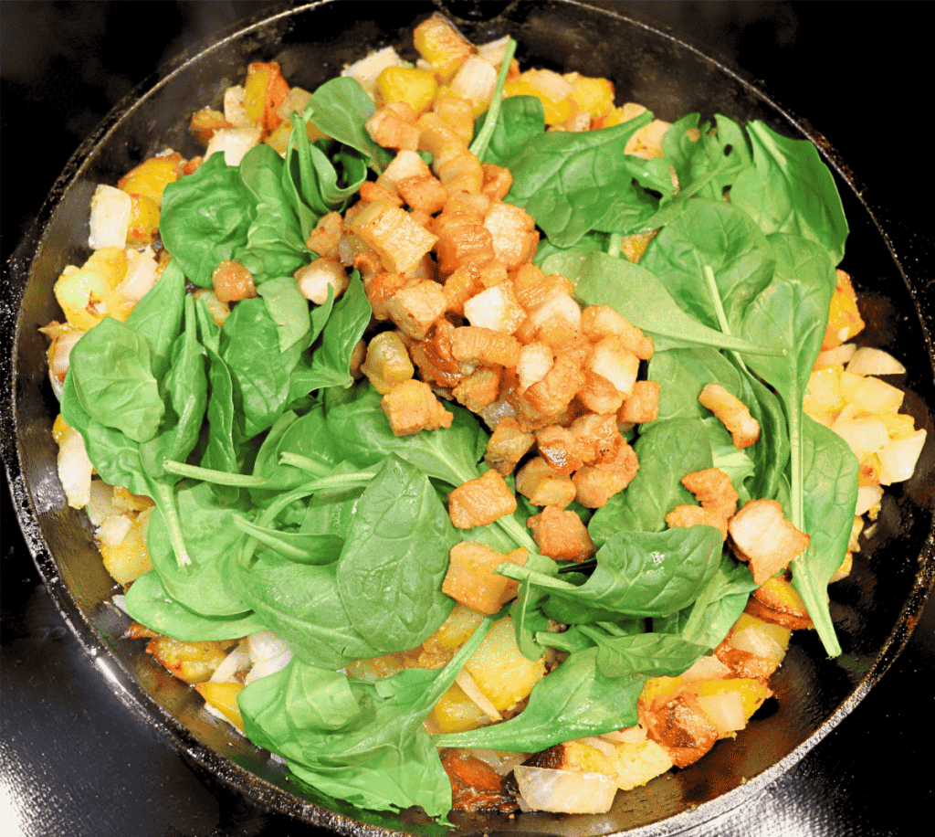 German potato skillet dish with spinach and cooked pork belly on top