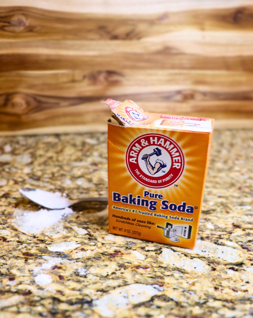 Open baking soda box on a counter with a spoonful of baking soda next to it.