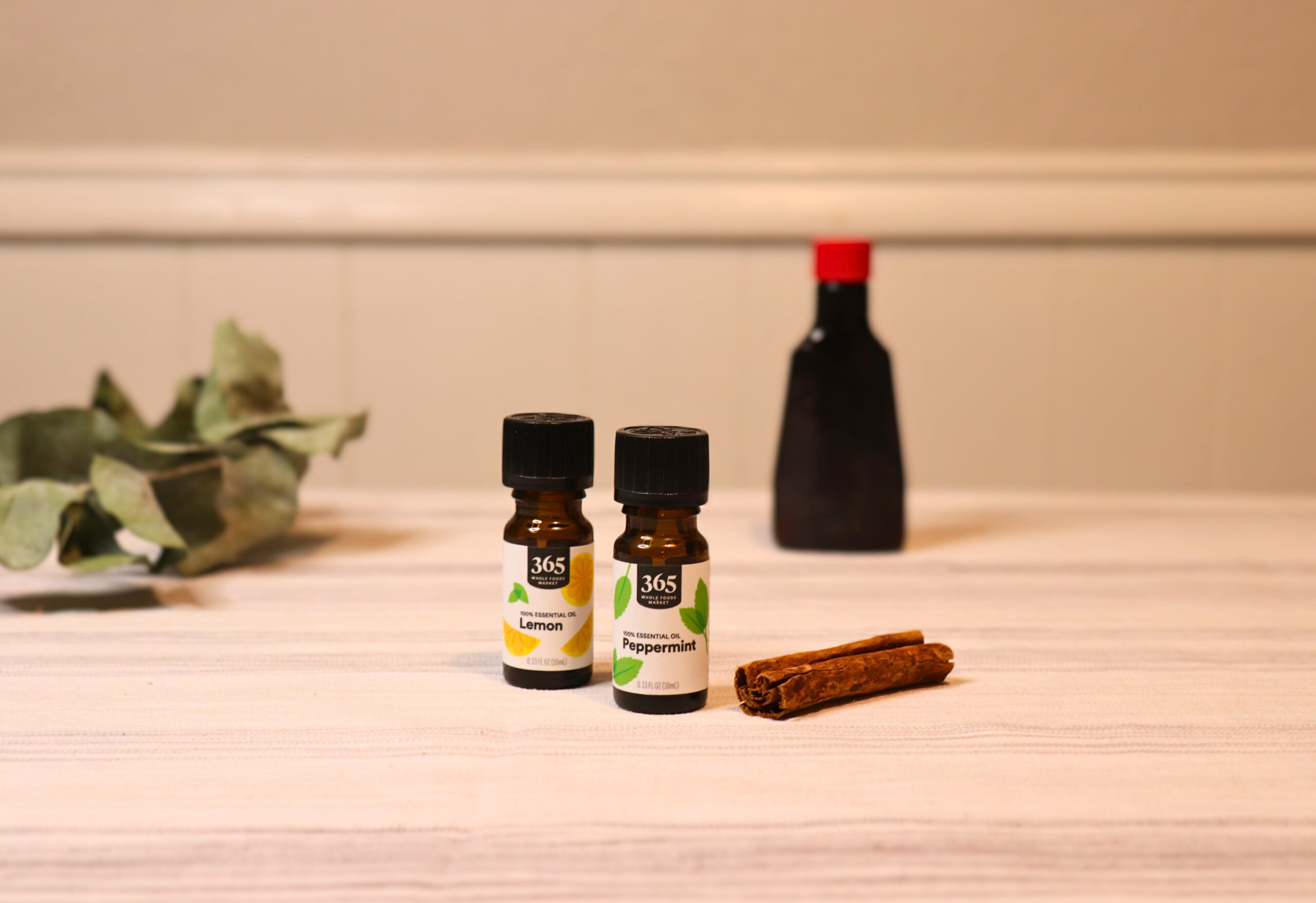 Two bottles of essential oil next to an unmarked bottle, a cinnamon stick, and some eucalyptus for natural cleaning