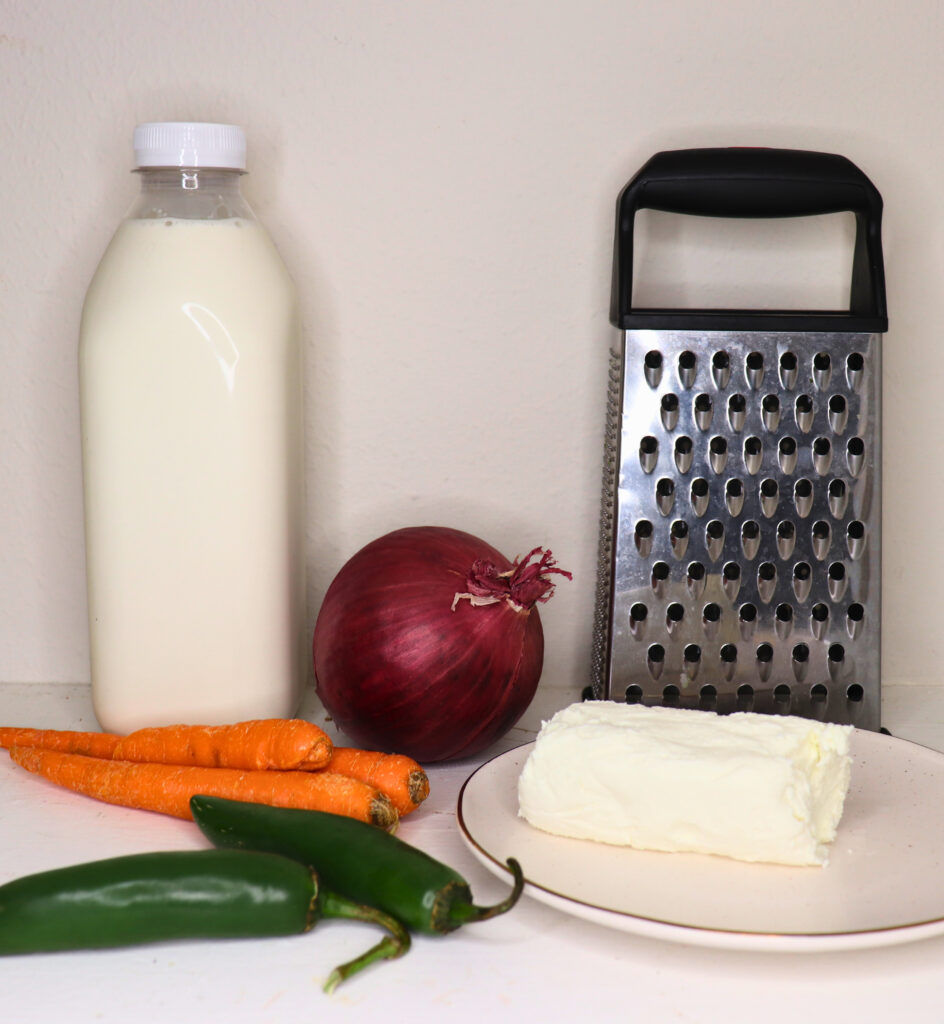 Milk, goat cheese, produce and a grater arranged together