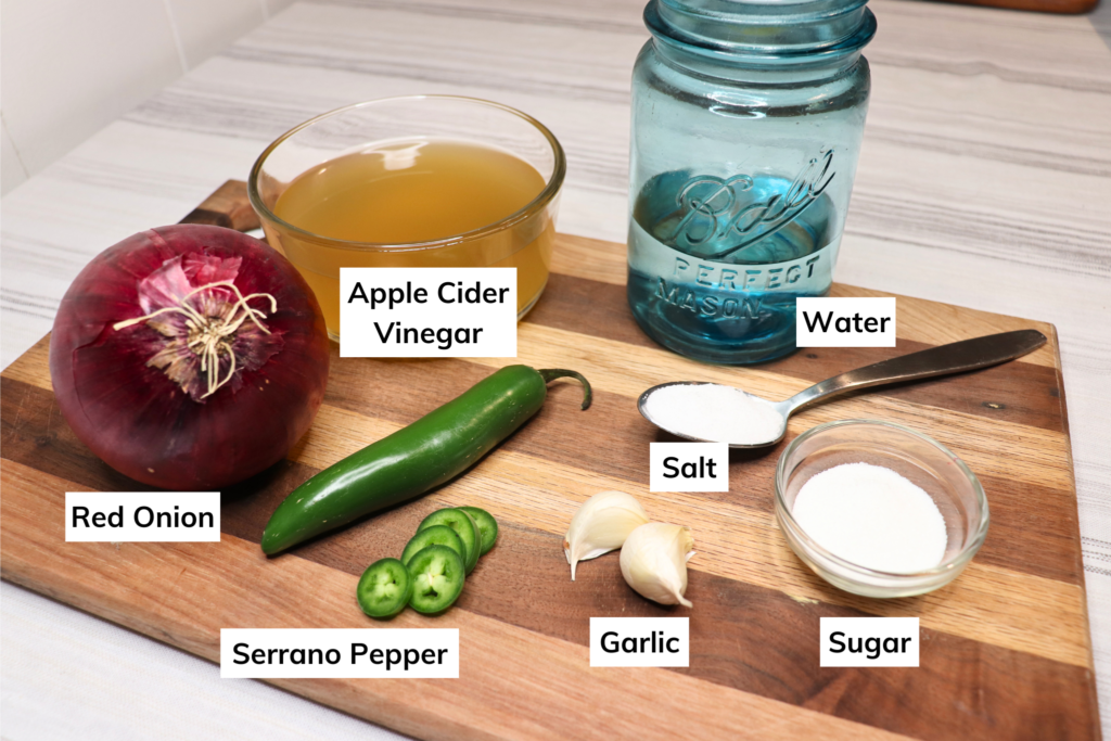 Ingredients for spicy pickled onions laid out on a wooden board