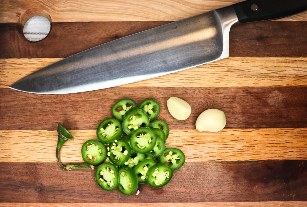 Sliced serrano pepper and garlic cloves on a wooden cutting board by a knife