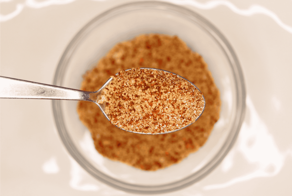 A spoonful of pork dry rub in focus with the bowl of rub blurred in the background.