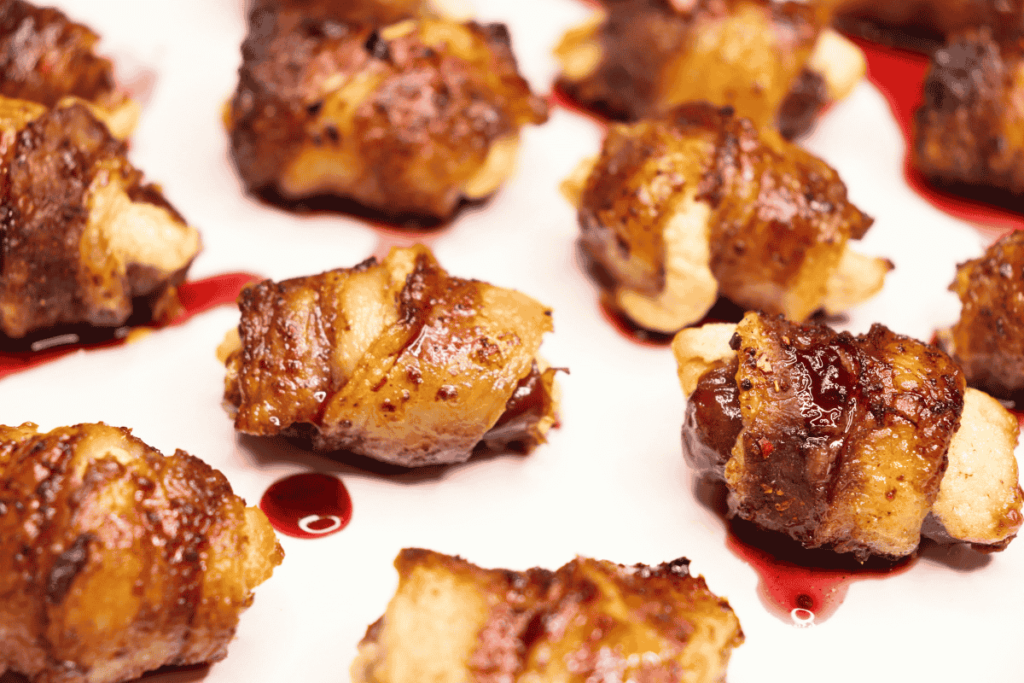 Bacon wrapped stuffed dates with a cherry sauce on a while plate