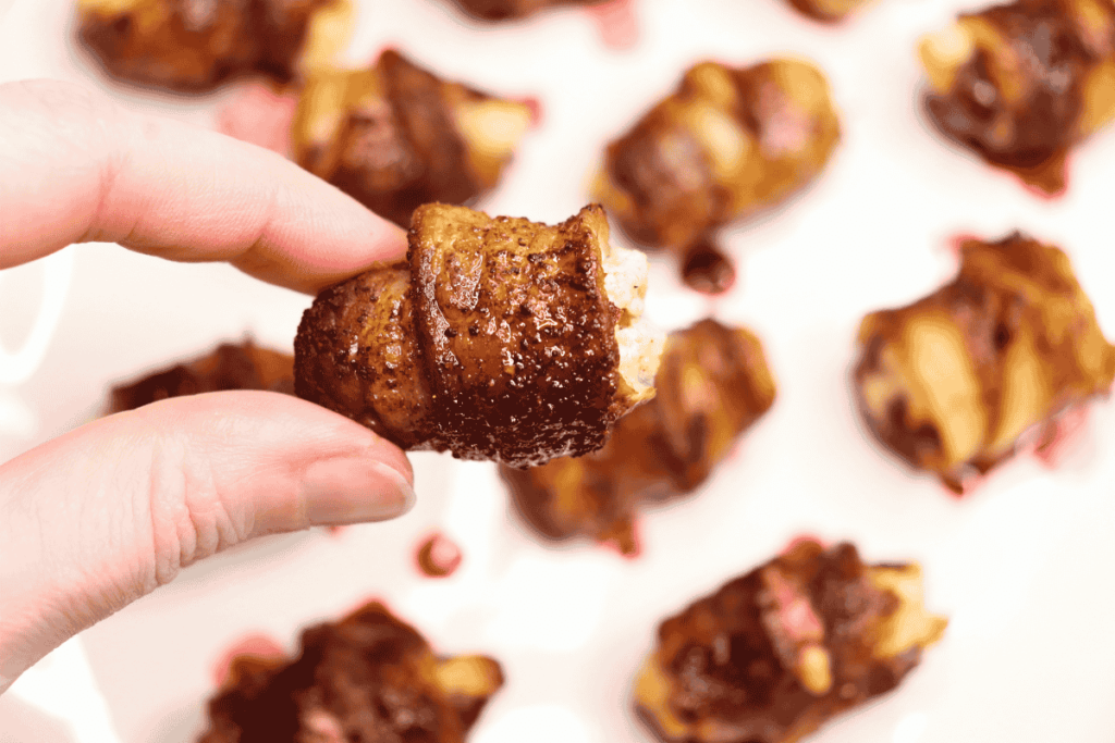 A bacon wrapped stuffed date appetizer held in focus with others behind it.