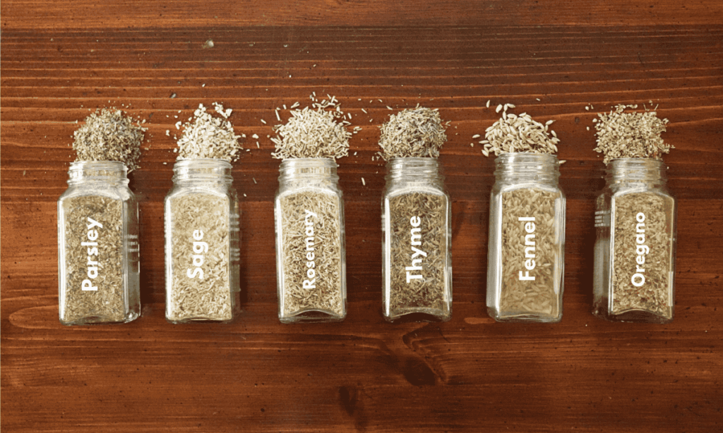 Spice bottles line up on a wooden table with herbs or spices pouring out