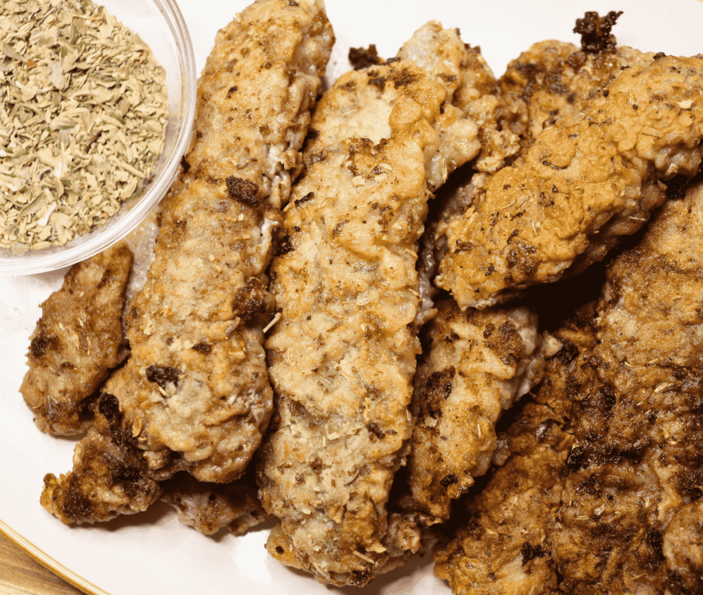 Beef steak fingers on a plate next to a bowl of dried herbs