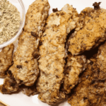 Beef steak fingers on a plate next to a bowl of dried herbs
