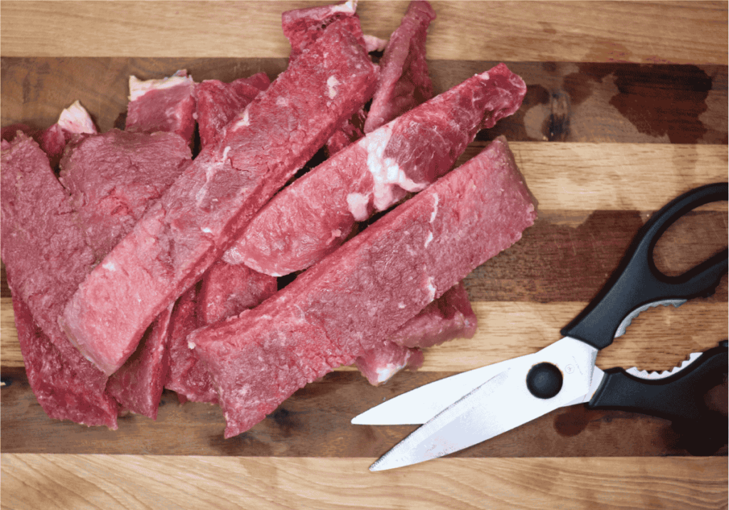 Beef cutlet cut into strips next to a pair of kitchen shears