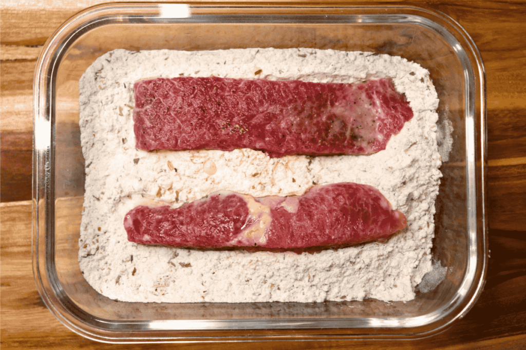 Beef strips in a bowl of flour for breading