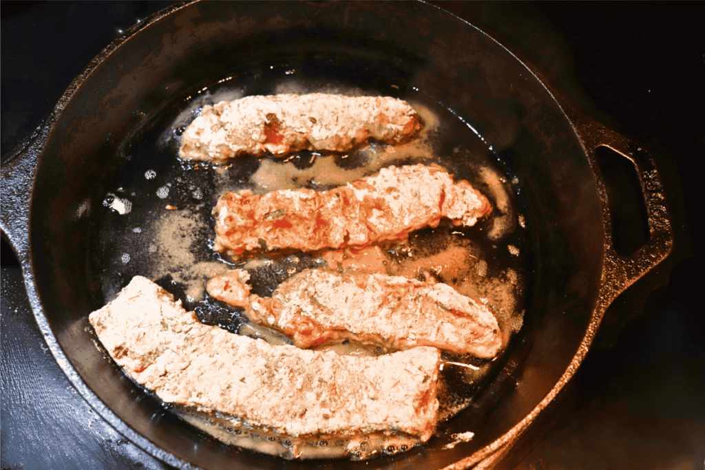 Breaded beef steak fingers frying in a cast iron skillet