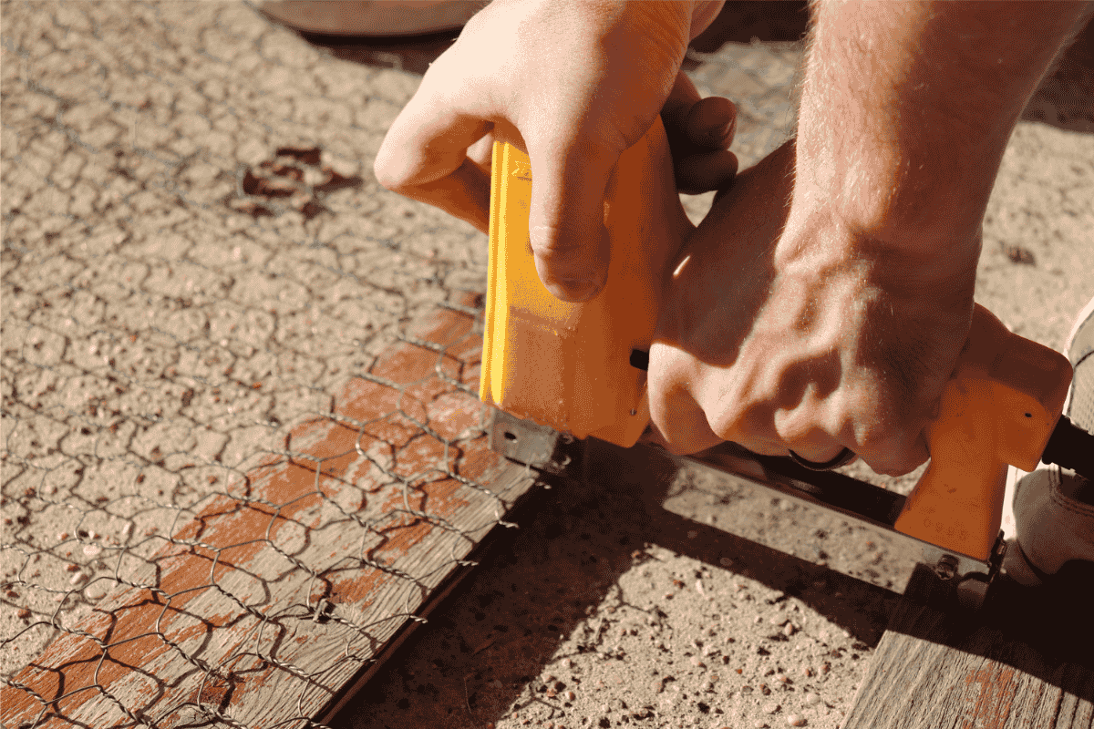 Stapling chickenwire to a garden stake with a yellow heavy duty stapler