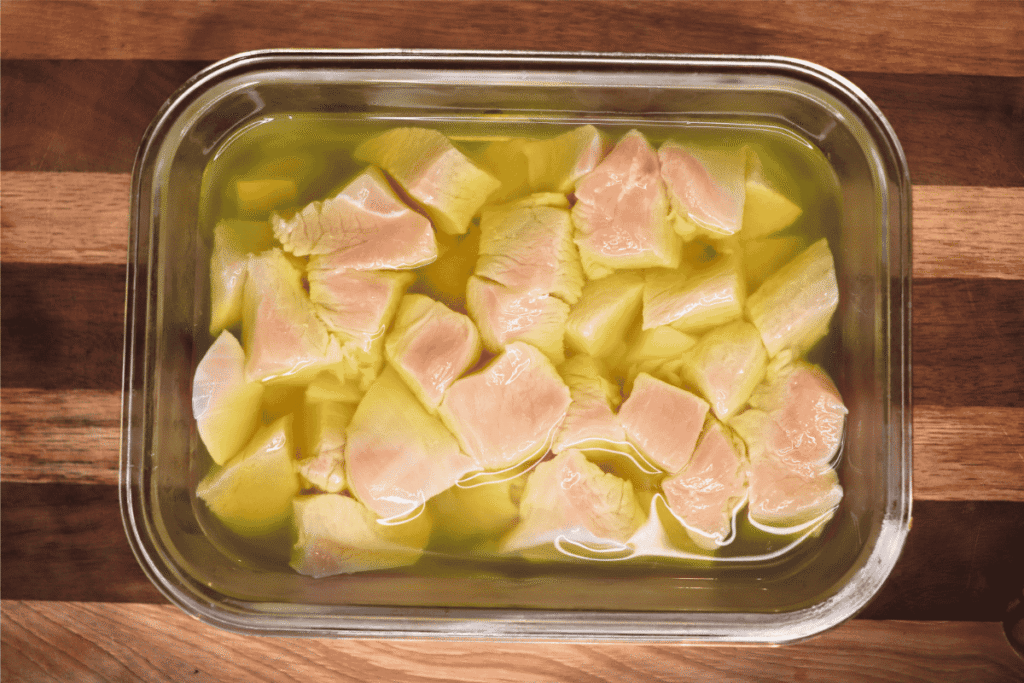 Pieces of chicken soaking in pickle juice in a glass casserole dish against a wooden background