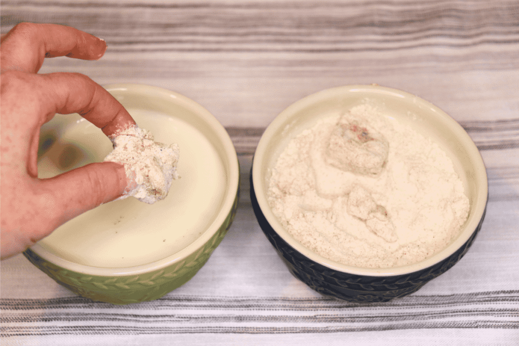 chicken nuggets being dipped in a bowl of milk and a bowl of flour mixture