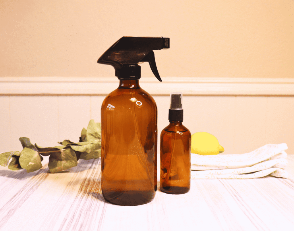 Two glass spray cleaner bottles on a white table cloth with eucalyptus and lemon in the background