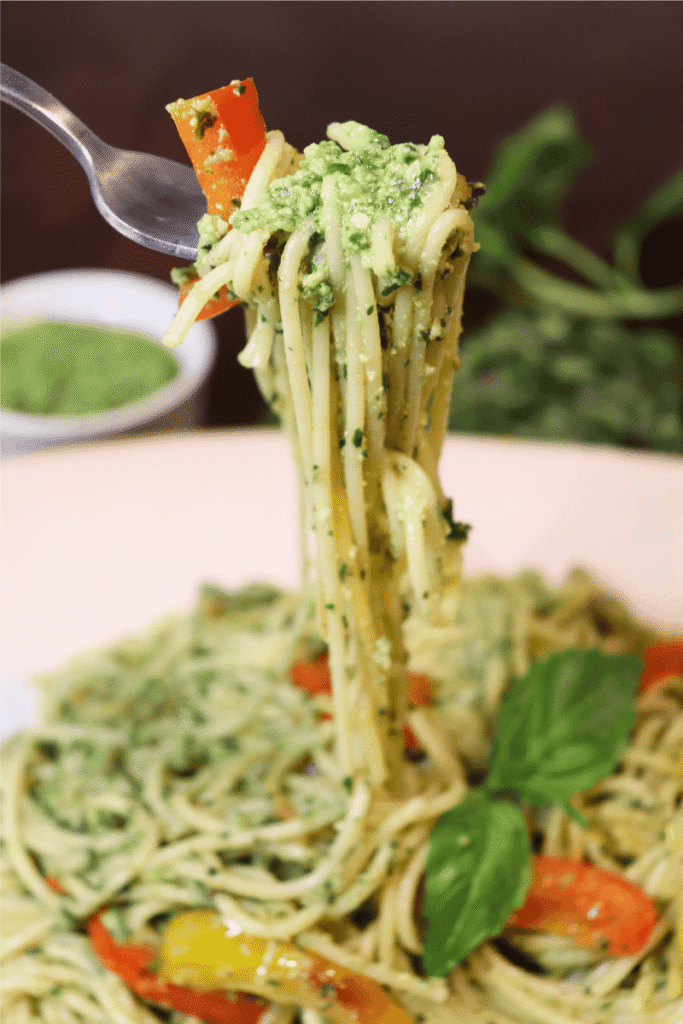A close-up of a bite of pesto pasta coming being lifted from a full plate