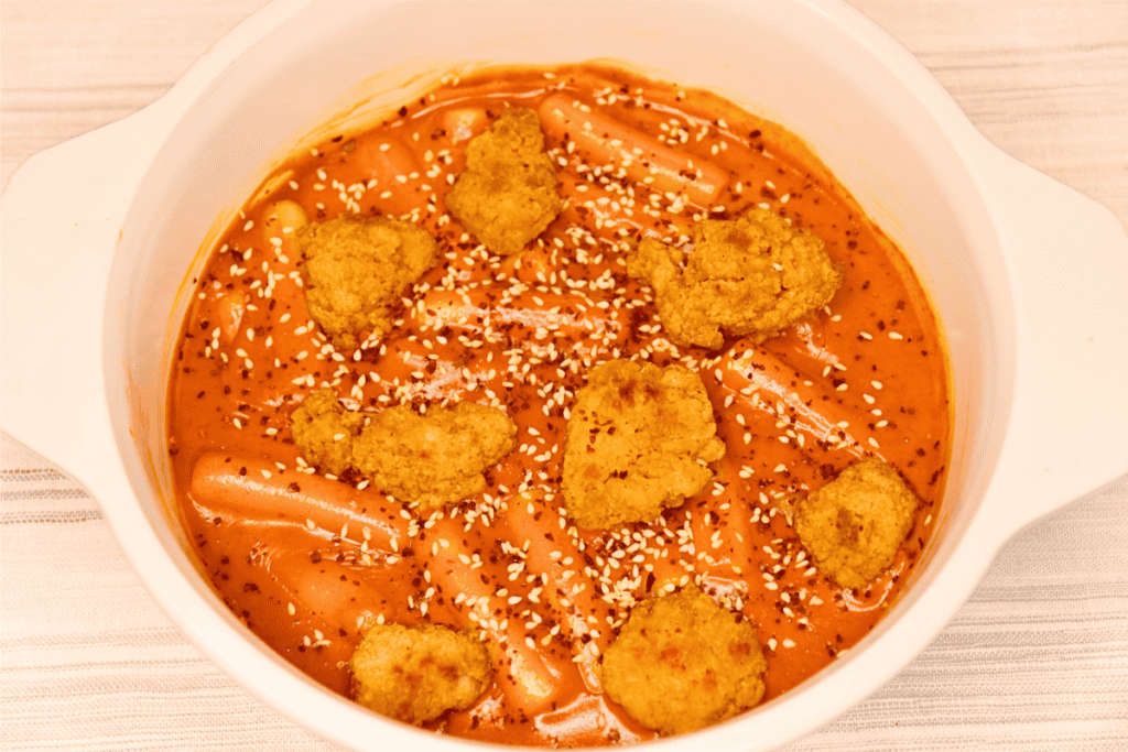 crispy chicken in creamy tteokbokki in a white ceramic dish