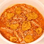 crispy chicken in creamy tteokbokki in a white ceramic dish