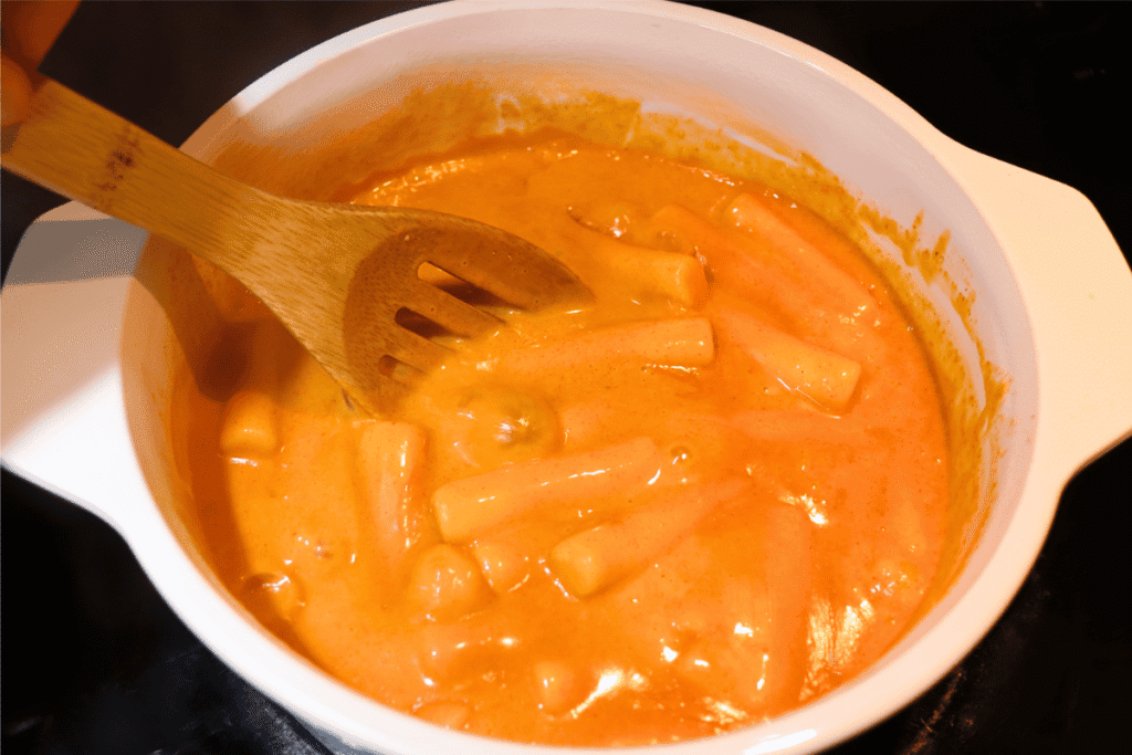 Stirring the creamy tteokbokki with a wooden spoon as it is simmering