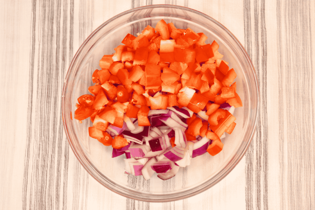 Chopped bell peppers, tomatoes, and red onion in a glass bowl