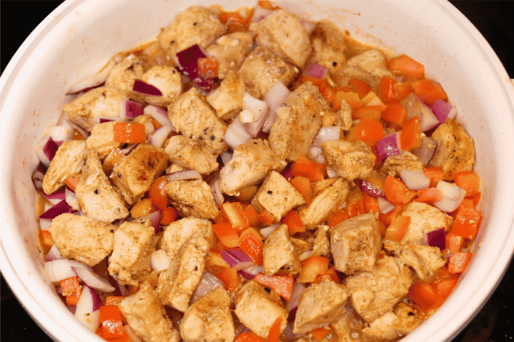 Chicken and vegetables cooking in a white, ceramic pan