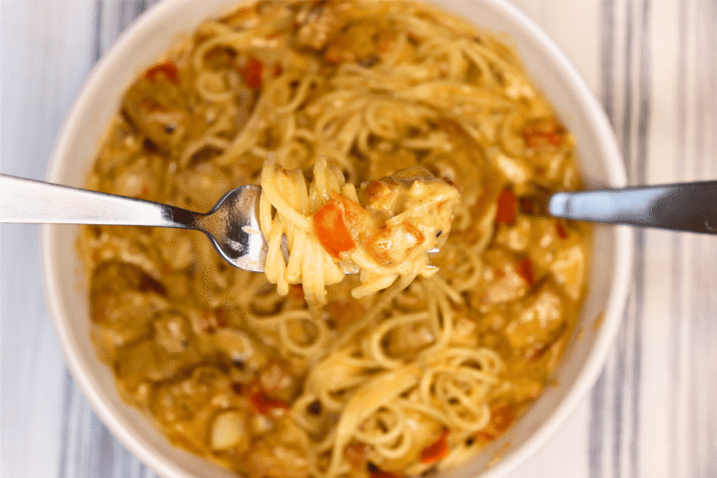 Close up shot of a forkful of Cajun Chicken Alfredo with the bowl below it in the background