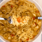 Close up shot of a bite of Cajun Chicken Alfredo with the bowl in the background