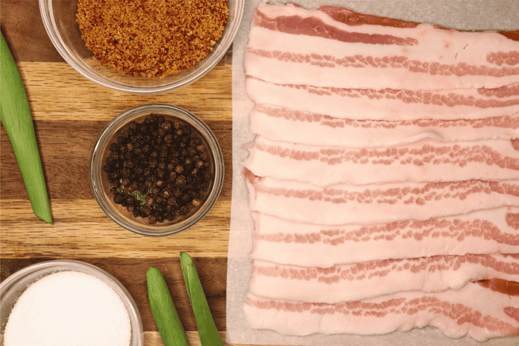 Sliced pork belly next to bowls of spices on a wooden board