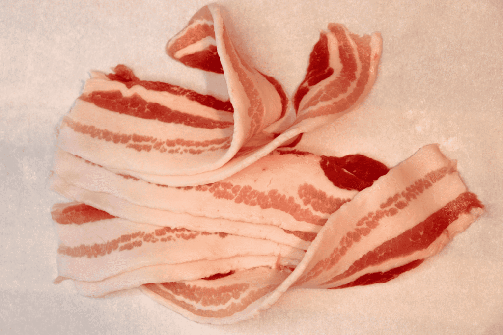 Raw pork belly sliced into bacon on parchment paper