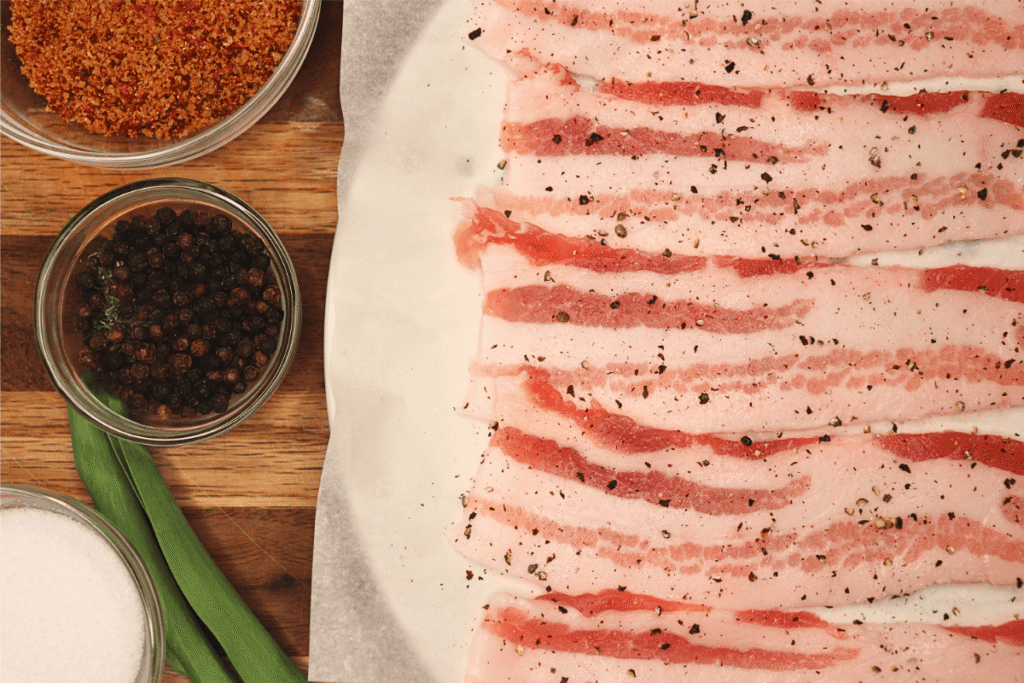 Sliced and seasoned pork belly next to small spice bowls