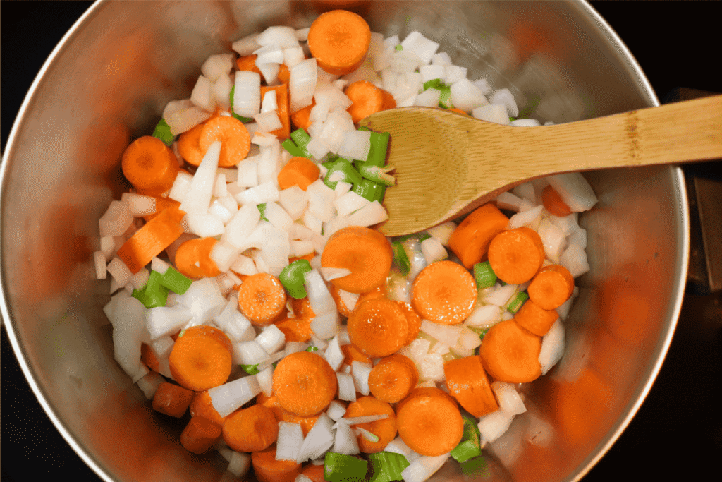Carrots, celery, and onions in a pot with a wooden spoon
