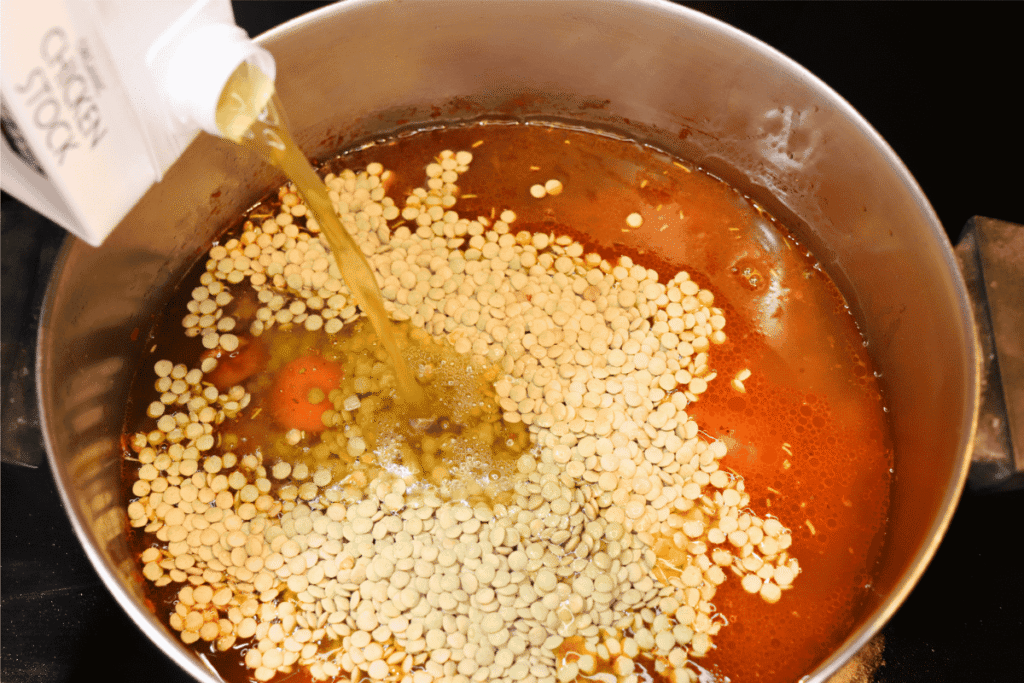 Pouring chicken broth into a pot of lentil soup