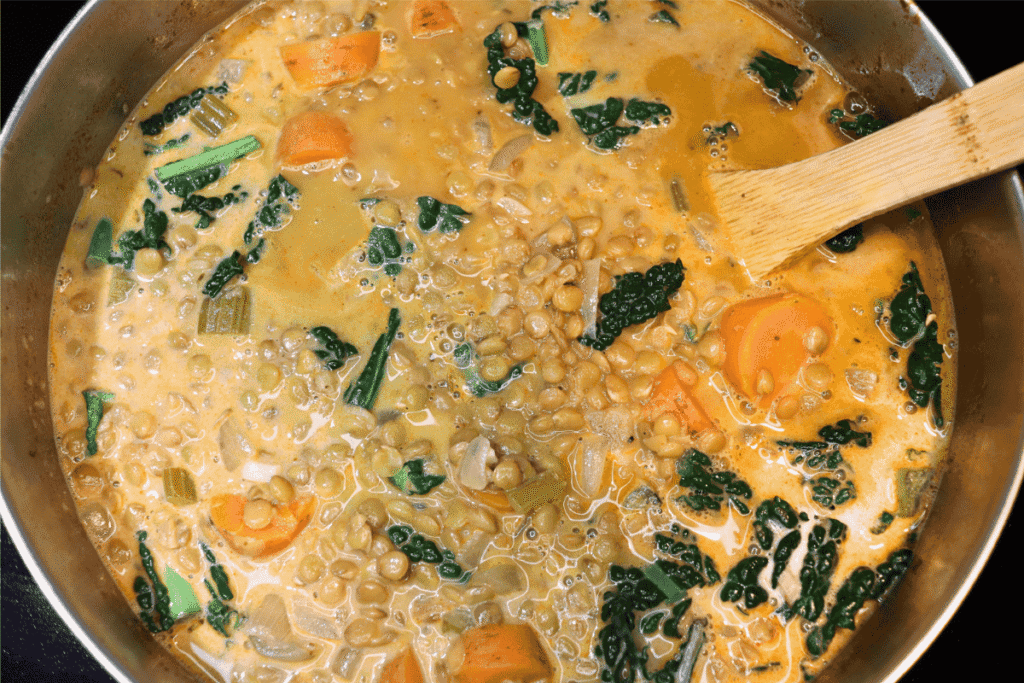 Kale cooking in a pot of soup and being stirred by a wooden spoon