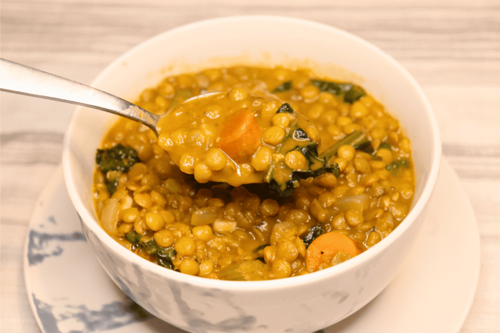 A close up of a spoonful of creamy lentil soup in a white bowl on a white tablecloth