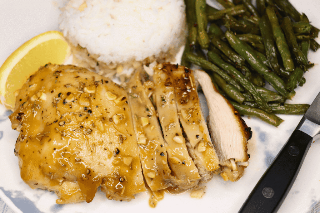 Sliced honey dijon chicken thigh on a plate with green beans, rice, and a knife