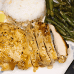 Sliced honey dijon chicken on a plate with green beans, rice, and a knife