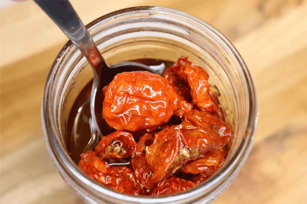 Sun-dried tomatoes in olive oil in a glass jar with a spoon