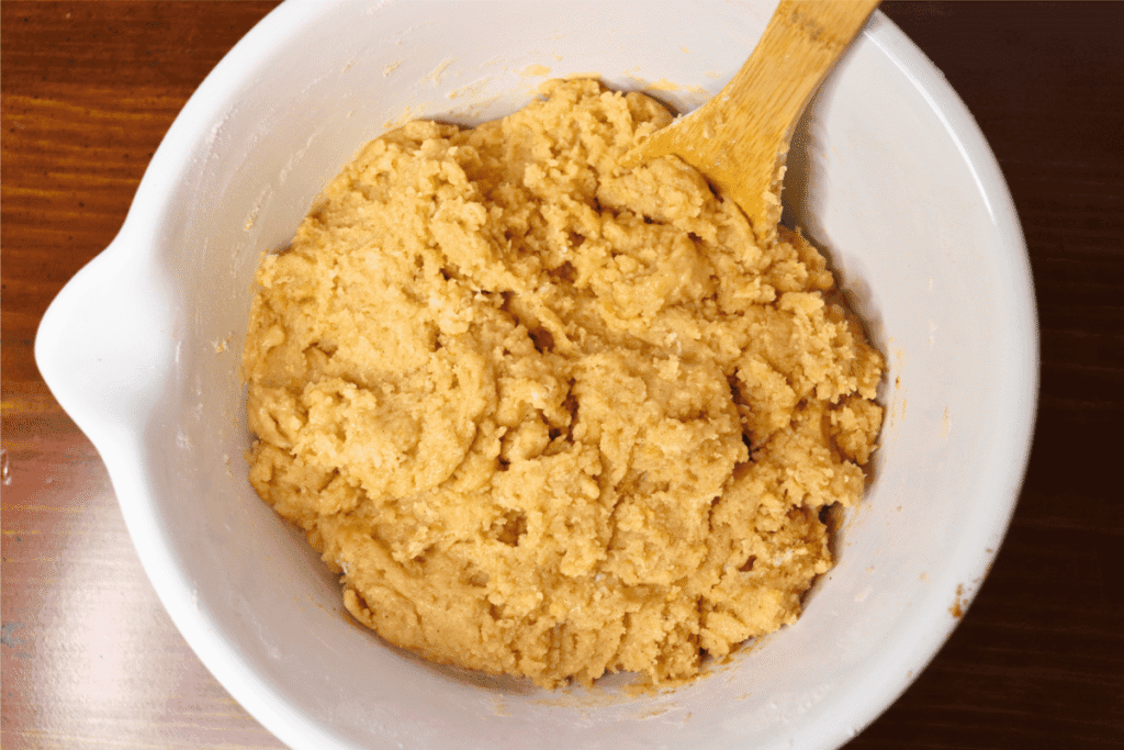 Large white bowl with mixed batter and a wooden spoon in it.