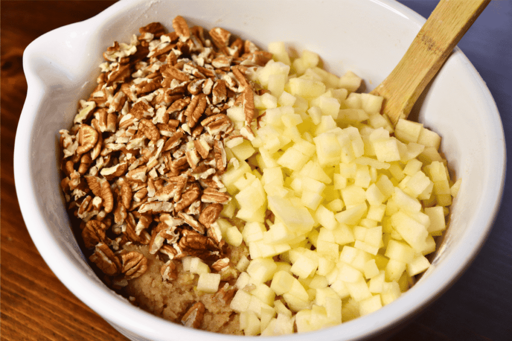 Large white bowl with batter, pecans, and chopped apples in it