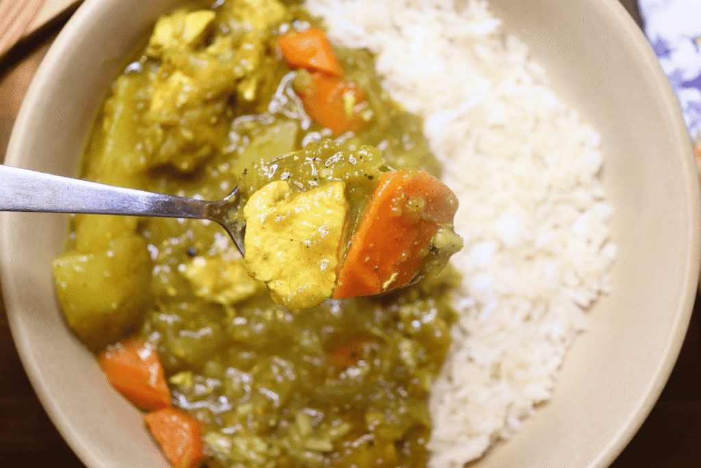 Close up of a spoonful of Japanese chicken curry with the bowl in the background