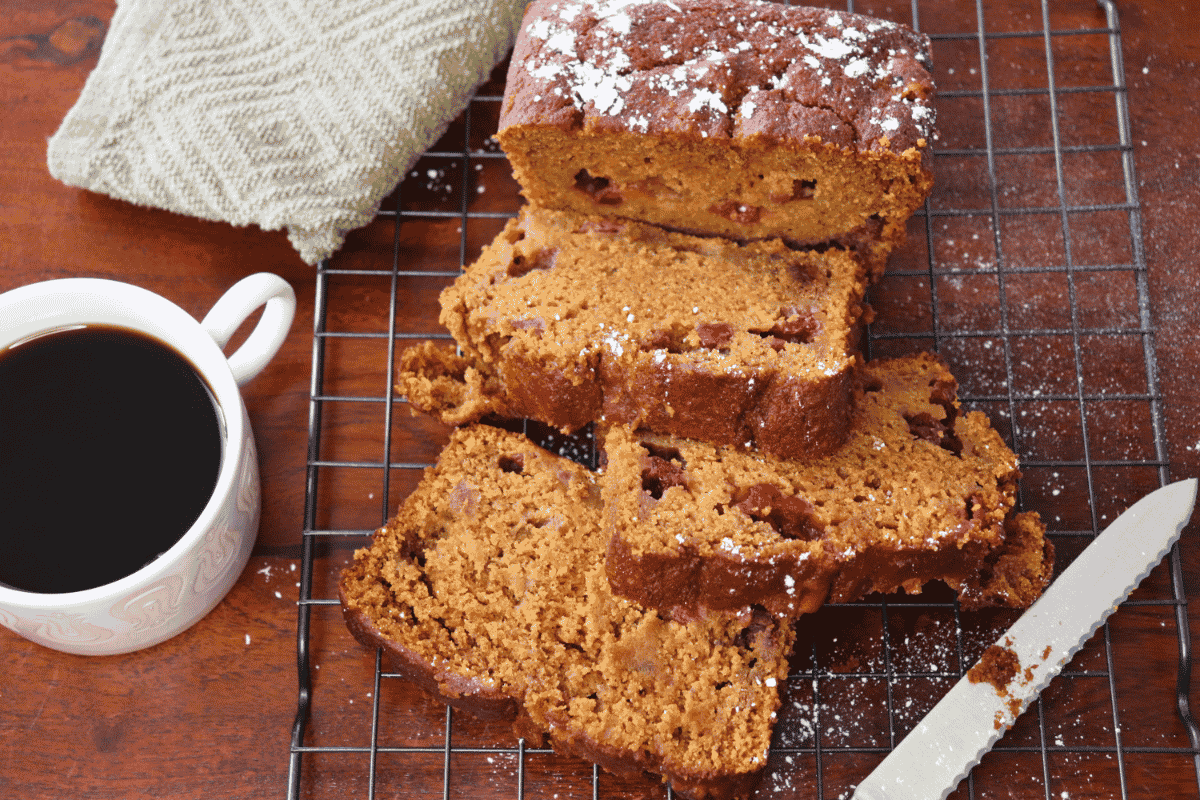 Sliced Pumpkin Cranberry Bread loaf on a cooling rack by a knife and cup of coffee