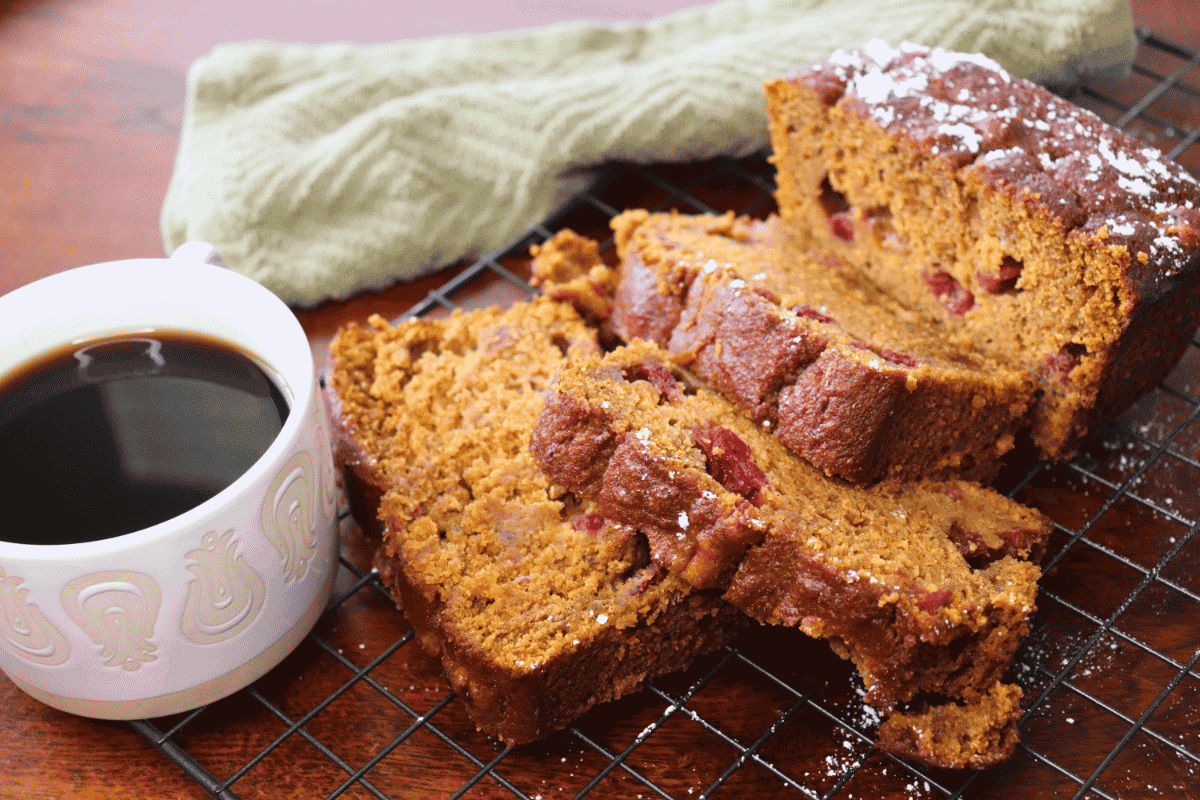 Sliced Pumpkin Cranberry Bread loaf next to a cup of coffee