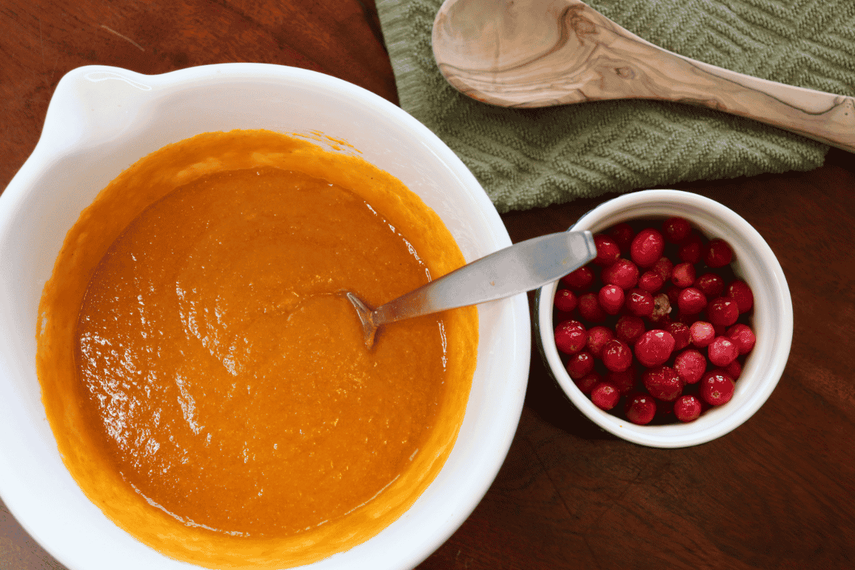 Large bowl of pumpkin puree next to a small bowl of whole cranberries