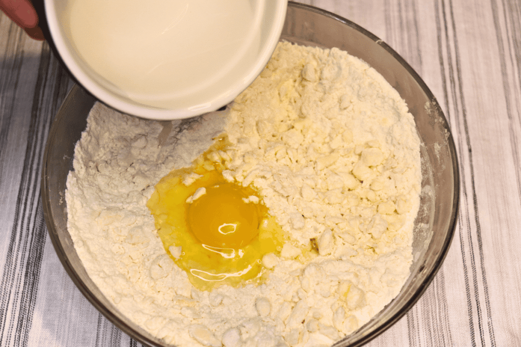 Adding egg, water, and vinegar to a mixing bowl full of flour and butter