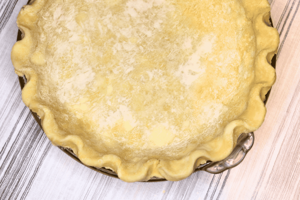 Raw homemade pie crust shaped in a pie dish on a white cloth